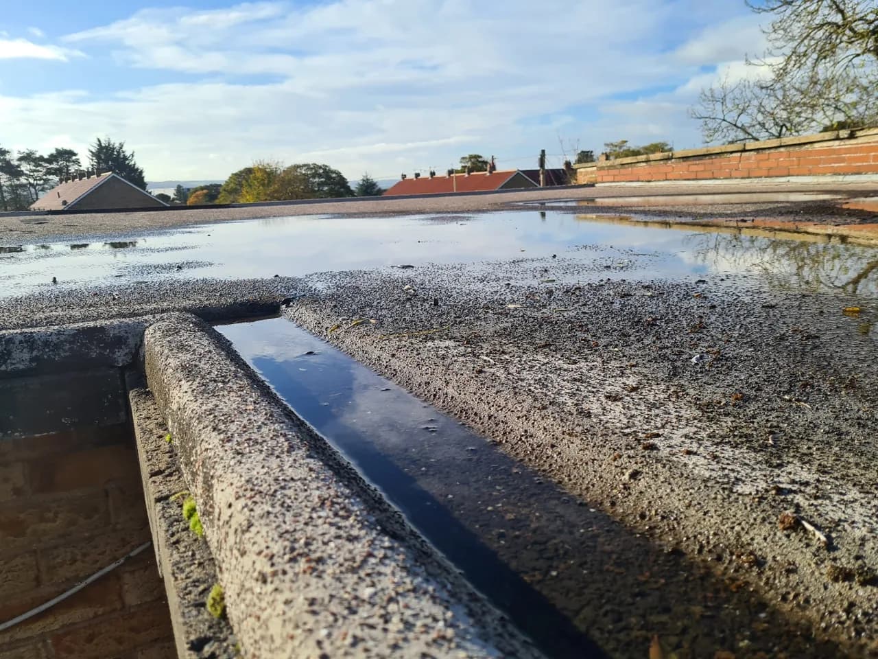 Existing porous flat roof covering at Eastfield Clinic showing standing water before liquid-applied waterproofing.
