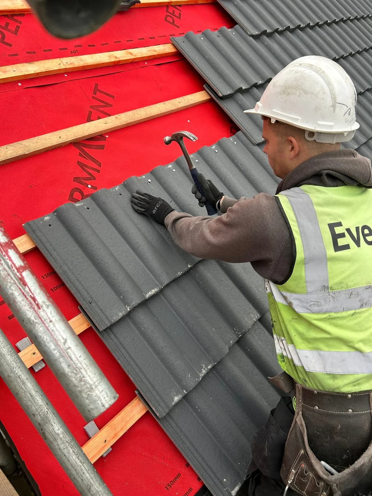 Evenii operative installing new tiles over red breather membrane during the roof replacement at 1-9 The Close, Cotherstone.