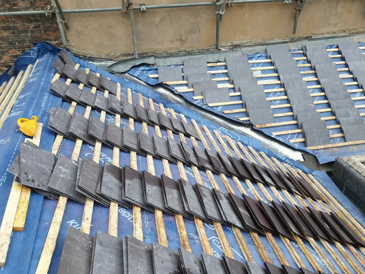 Welsh slate stacked on new battens and breather membrane across the prepared Trinity House roof slope during installation.
