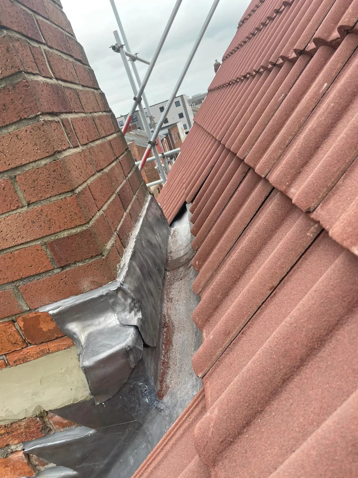 Completed pitched roof in red interlocking pantiles with lead soakers at the chimney abutment — pitched roof replacement County Durham