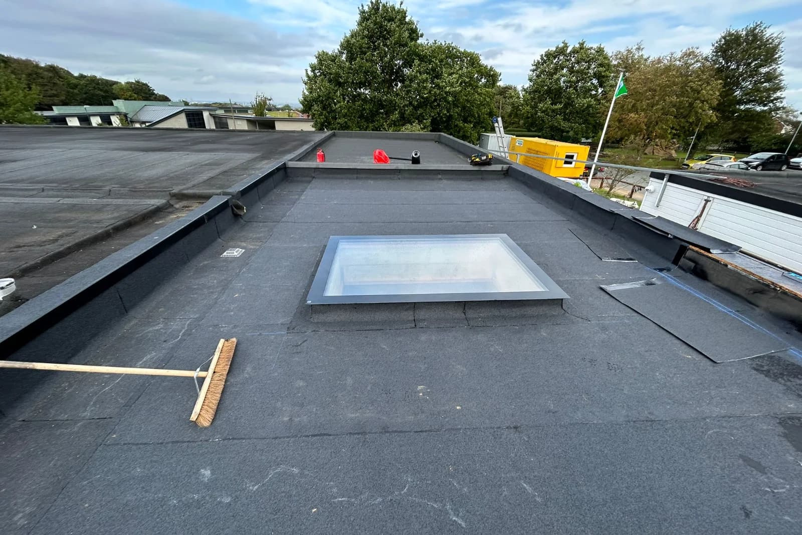 Completed flat felt roof on a school building with hillside backdrop and parapet upstand — roofing contractor for schools and academies